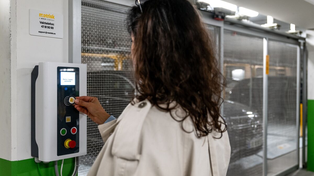 Una persona utiliza el panel de control de un sistema de aparcamiento semiautomático para recuperar un vehículo estacionado. Al fondo se pueden ver las plazas de aparcamiento móviles y un vehículo dentro de la instalación de estacionamiento.