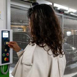 Una persona utiliza el panel de control de un sistema de aparcamiento semiautomático para recuperar un vehículo estacionado. Al fondo se pueden ver las plazas de aparcamiento móviles y un vehículo dentro de la instalación de estacionamiento.