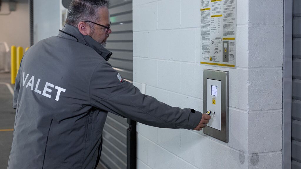 L’image montre une personne devant le panneau de commande d’un système de stationnement automatisé, confirmant le processus de stockage et lançant ainsi le transport automatique du véhicule vers une place de stationnement disponible.