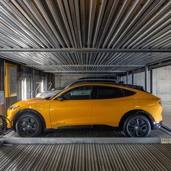 L’image montre une voiture sur une plateforme à l’intérieur d’un système de stationnement automatisé dans un parking souterrain moderne.