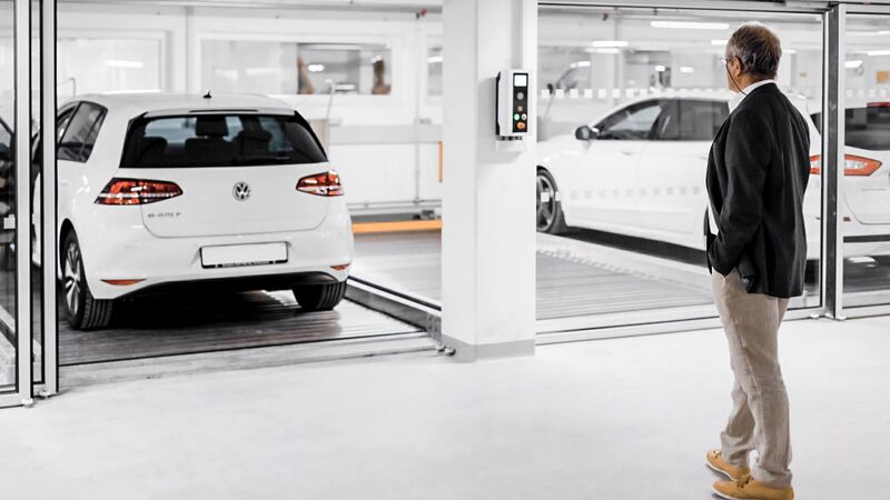 A man stands in front of a parking system with cars