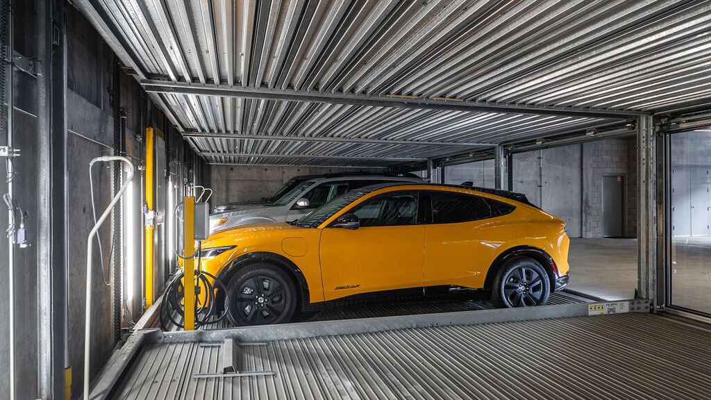 L’image montre une voiture sur une plateforme à l’intérieur d’un système de stationnement automatisé dans un parking souterrain moderne.