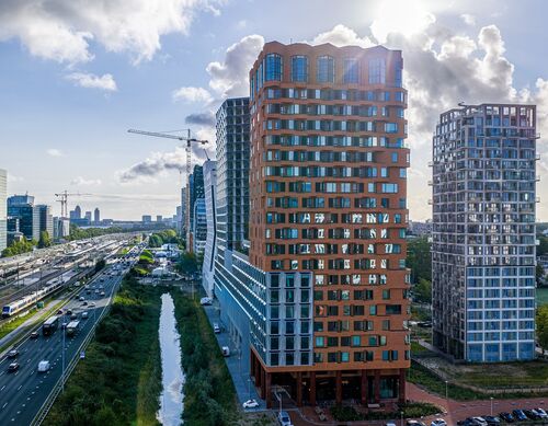 Vista exterior del proyecto The Pulse en Ámsterdam con modernos edificios de gran altura e infraestructura de transporte urbano.