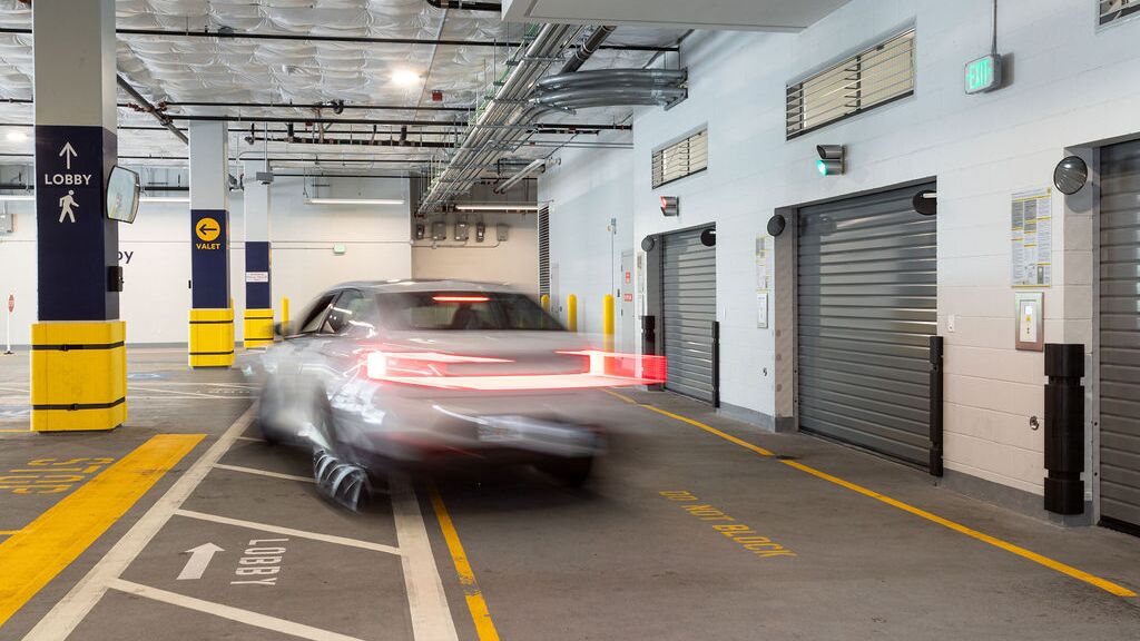 L’image montre un véhicule entrant dans un système de stationnement automatisé au sein d’un parking souterrain moderne avec plusieurs portes d’accès.