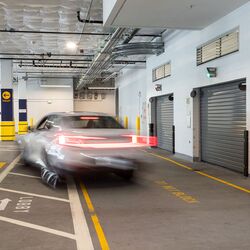 L’image montre un véhicule entrant dans un système de stationnement automatisé au sein d’un parking souterrain moderne avec plusieurs portes d’accès.