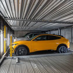 L’image montre une voiture sur une plateforme à l’intérieur d’un système de stationnement automatisé dans un parking souterrain moderne.